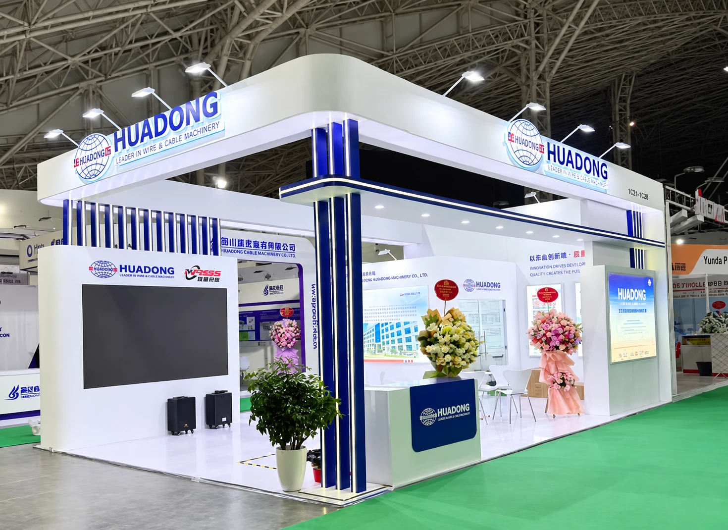 White and blue HUADONG packaging exhibition booth with overhead branding, a large screen and open seating