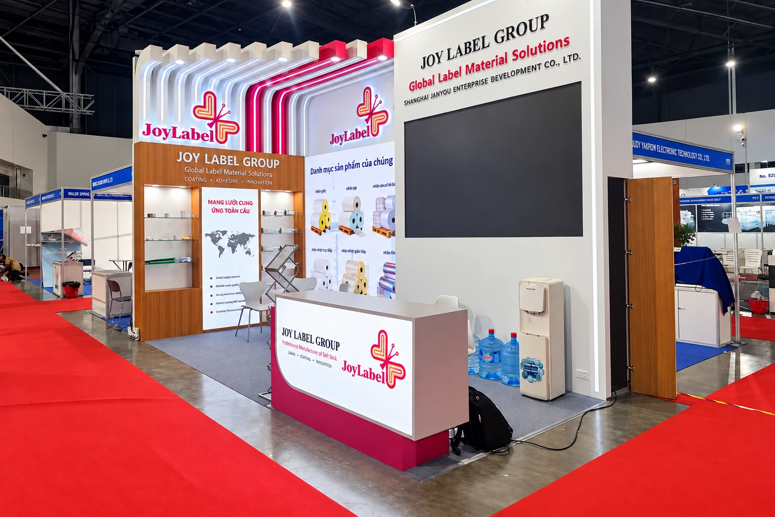 Joy Label Group booth with layered white and magenta frames, a large screen and a product information counter