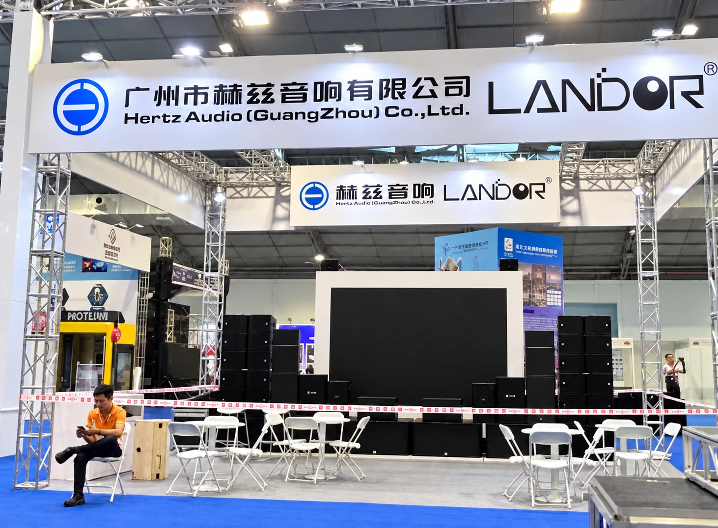 LANDOR and Hertz Audio booth with white overhead company signage, speakers, display equipment and meeting chairs